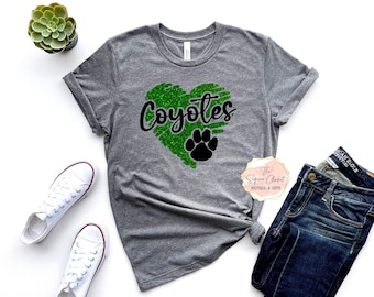 May include: A gray t-shirt with a green glitter heart that says "Coyotes" in black lettering. A black paw print is inside the heart.