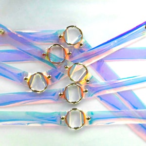 May include: A set of iridescent clear plastic choker necklaces with gold metal rings and studs. The necklaces are layered and overlapping.