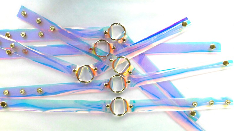 May include: A set of iridescent clear plastic choker necklaces with gold metal rings and studs. The necklaces are layered and overlapping.