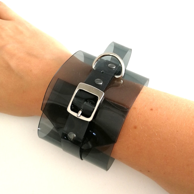May include: A black plastic bracelet with a silver buckle and a clear plastic overlay.