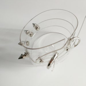 May include: A clear plastic bracelet with silver spikes and a silver clasp.