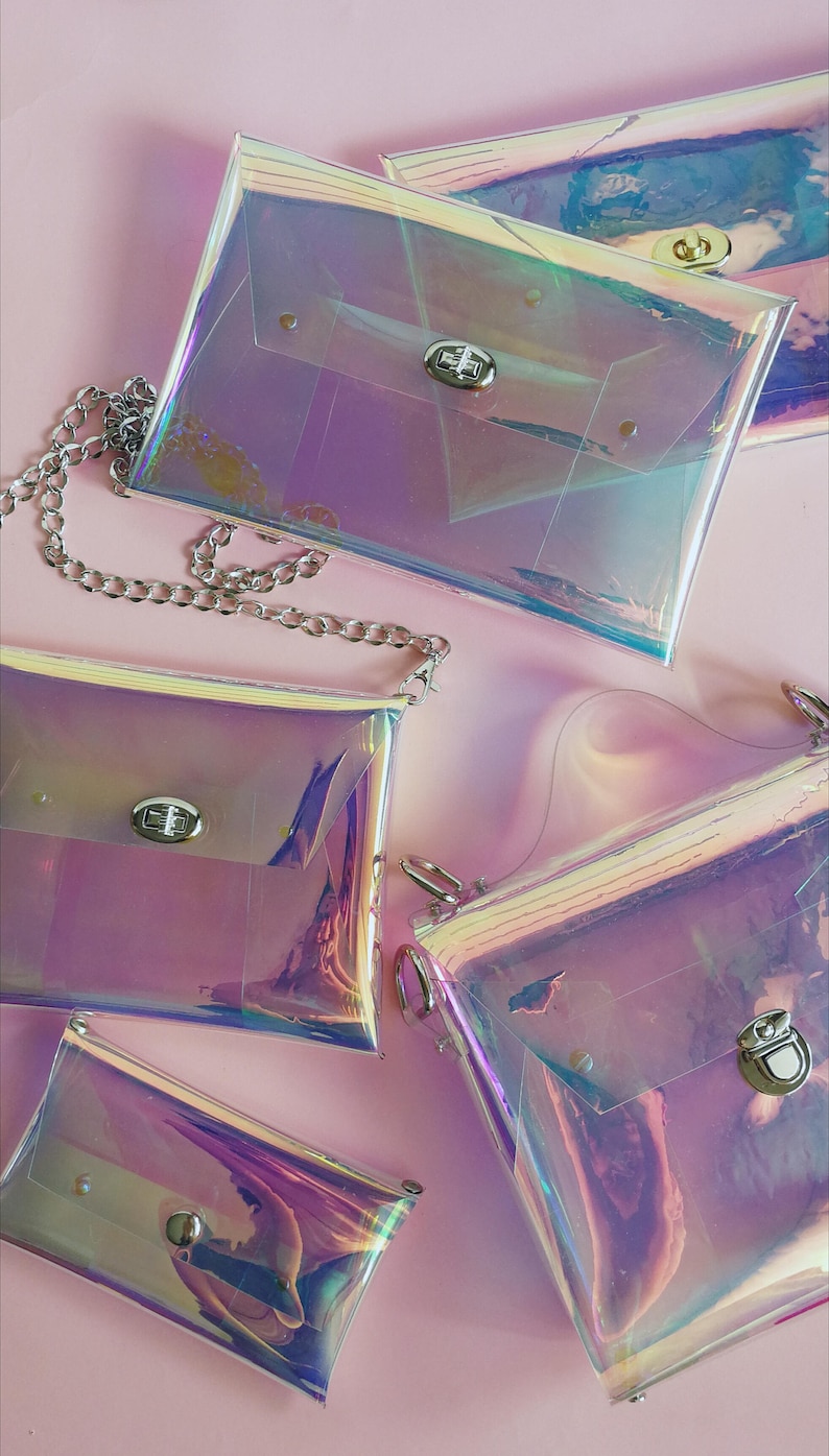 May include: Four iridescent clear plastic purses with silver clasps and a silver chain. The purses are on a pink background.