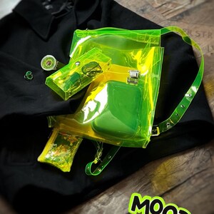 May include: A neon green transparent backpack with a matching small pouch and a black coat. The backpack has a yellow interior and a green pocket. A small green ring and a watch are also visible. The word "MOOD" is in a green and yellow sticker.