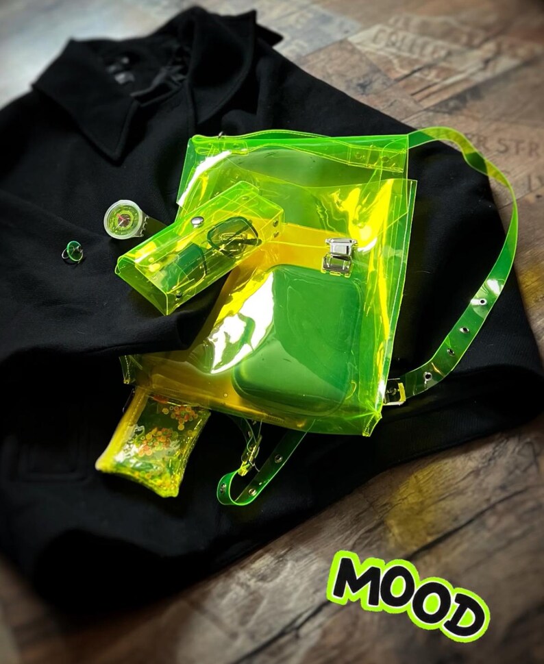 May include: A neon green transparent backpack with a matching small pouch and a black coat. The backpack has a yellow interior and a green pocket. A small green ring and a watch are also visible. The word "MOOD" is in a green and yellow sticker.