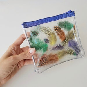 Puede incluir: Una bolsa transparente de pl&aacute;stico con cremallera azul y una variedad de plumas de colores en su interior.