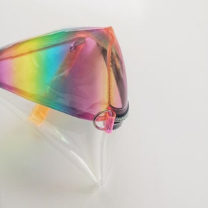 May include: A clear plastic zippered pouch with a rainbow iridescent design. The pouch has a pink zipper pull and a silver ring.