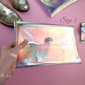 May include: A iridescent holographic clutch purse with a silver clasp. The purse is held in a hand and the text "Size 3" is visible in the background.