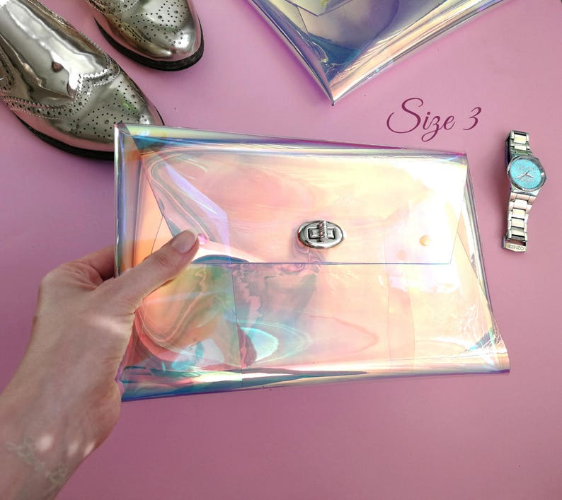 May include: A iridescent holographic clutch purse with a silver clasp. The purse is held in a hand and the text "Size 3" is visible in the background.
