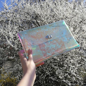 May include: A clear iridescent clutch bag with a silver clasp. The bag is made of a plastic material and has a holographic finish.