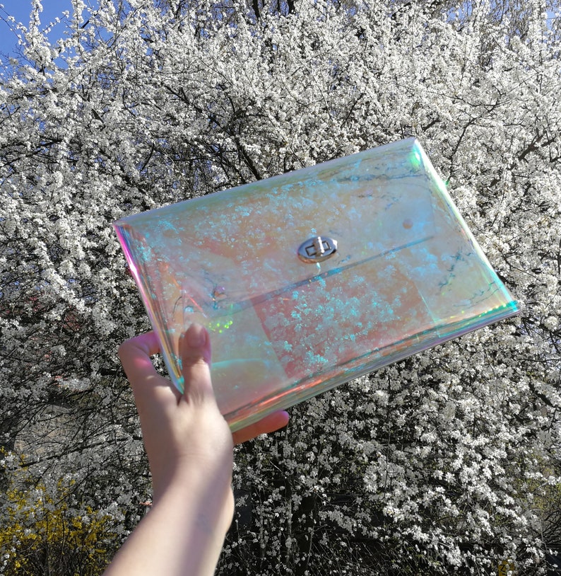May include: A clear iridescent clutch bag with a silver clasp. The bag is made of a plastic material and has a holographic finish.