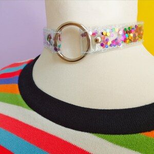 Op de afbeelding: Een transparante choker ketting met een zilveren ring sluiting. De ketting is versierd met kleurrijk confetti.