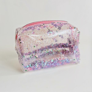 May include: Clear plastic cosmetic bag with a pink zipper and filled with iridescent pink and green glitter and sequins.