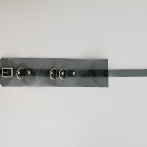 May include: A black leather choker with silver hardware, including a buckle, two D-rings, and three studs. The choker is transparent and has a black strap.