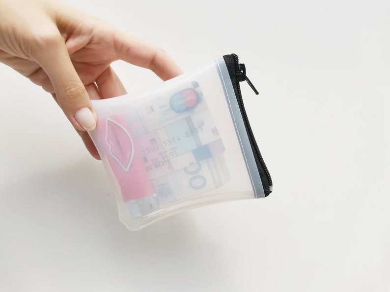 Puede incluir: Una bolsa transparente de pl&aacute;stico con cremallera negra. La bolsa contiene una tarjeta de cr&eacute;dito, dinero en efectivo y un b&aacute;lsamo labial rosa.
