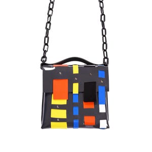 Könnte beinhalten: Eine schwarze Lederschultertasche mit einer Kettenkette und einem bunten geometrischen Muster in Rot, Gelb, Blau und Weiß.