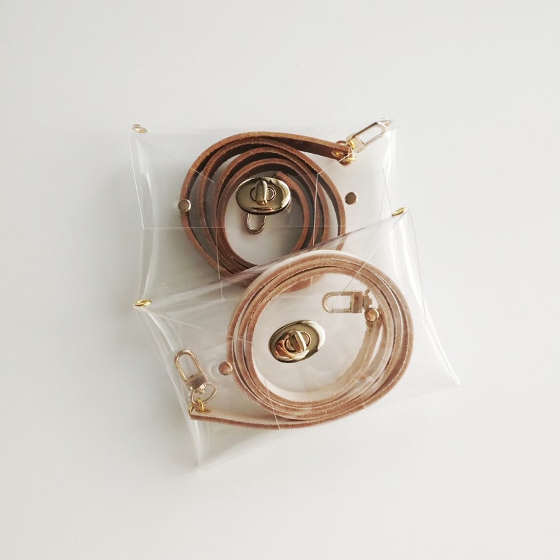 May include: Two clear plastic bags containing brown leather straps with gold clasps. The straps are coiled inside the bags.