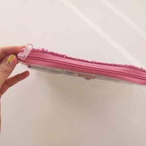 Pu&ograve; includere: Un astuccio rosa con un corpo in plastica trasparente e una cerniera rosa. L'astuccio &egrave; rettangolare e sembra essere parzialmente pieno. Il tirazip &egrave; anch'esso rosa.