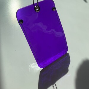 May include: A purple plastic keychain with a silver chain. The keychain is transparent and has a stitched border.