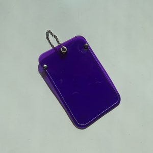 May include: A purple plastic card holder with a silver chain attached. The holder has a white stitched border.