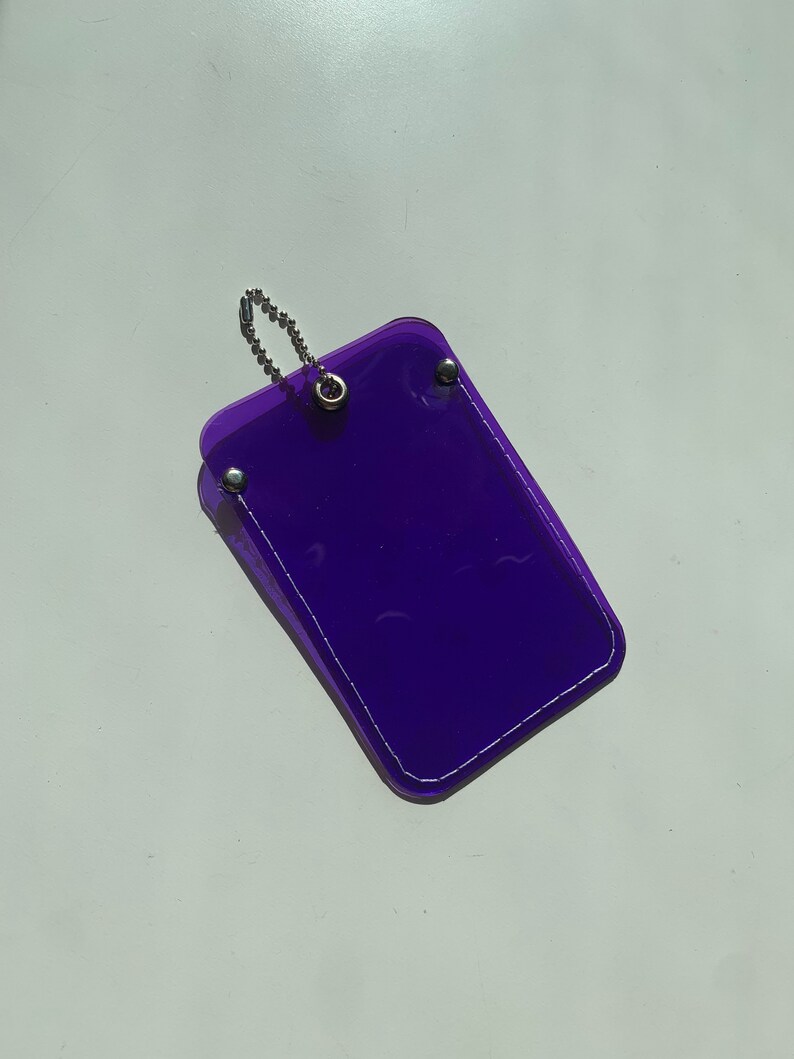 May include: A purple plastic card holder with a silver chain attached. The holder has a white stitched border.