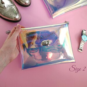 May include: A clear iridescent holographic purse with a silver chain strap and a silver clasp. The purse is held in a hand against a pink background. The text "Size 2" is visible in the bottom right corner of the image.