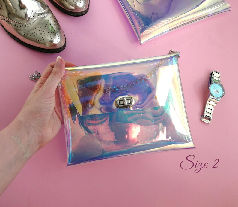 May include: A clear iridescent holographic purse with a silver chain strap and a silver clasp. The purse is held in a hand against a pink background. The text "Size 2" is visible in the bottom right corner of the image.