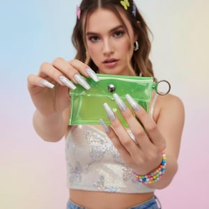 May include: A transparent neon green cardholder with a silver metal ring. The cardholder is held up by a person with long, silver glitter nails. The person is wearing a white top with a butterfly design and a colorful beaded bracelet.