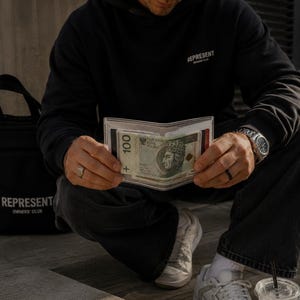 May include: A clear, transparent plastic wallet holding a 100 Polish Zloty banknote featuring a portrait of King Wladyslaw II Jagiello. The wallet is held open, displaying the currency clearly within its rectangular, minimalist frame.
