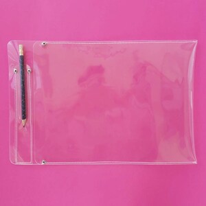 May include: A clear plastic document holder with a pencil in a pocket, set against a bright pink background. The holder has a rectangular shape with rounded corners and is secured with metal rivets.