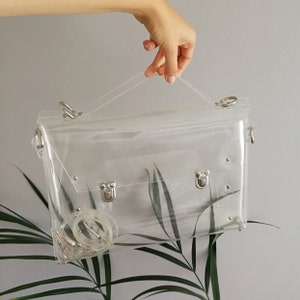 May include: A clear plastic satchel bag with silver hardware and a detachable shoulder strap.