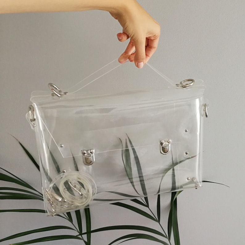 May include: A clear plastic satchel bag with silver hardware and a detachable shoulder strap.