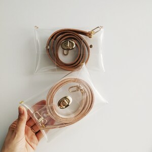 May include: Two clear plastic bags with brown leather straps and gold clasps. The straps are coiled inside the bags.