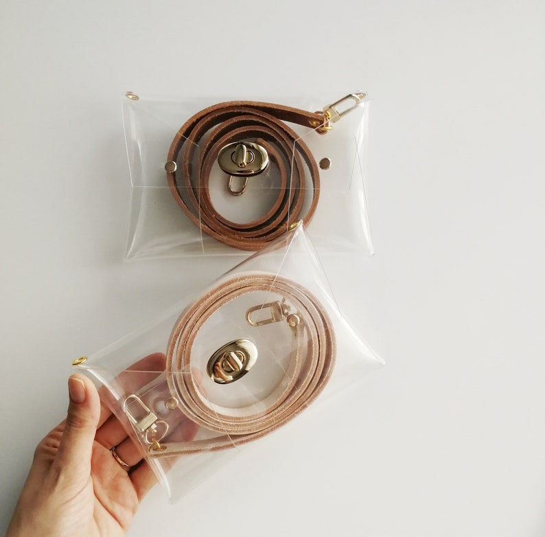May include: Two clear plastic bags with brown leather straps and gold clasps. The straps are coiled inside the bags.