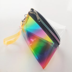May include: A clear iridescent rainbow cosmetic bag with a black zipper and a yellow strap.