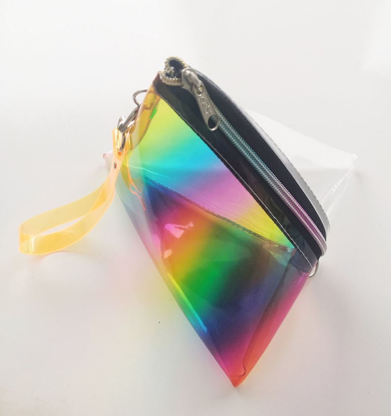 May include: A clear iridescent rainbow cosmetic bag with a black zipper and a yellow strap.