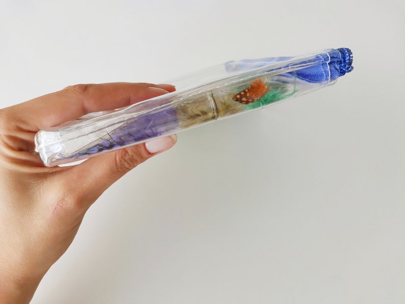 Puede incluir: Una bolsa de pl&aacute;stico transparente con un forro de tela azul. La bolsa contiene una variedad de flores secas y una peque&ntilde;a mariposa naranja.
