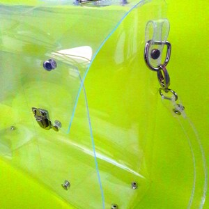 May include: A clear plastic tote bag with a silver chain strap. The bag has a flap closure with a silver buckle.