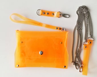 May include: An orange, translucent clutch bag with a matching wrist strap and a silver chain strap. The clutch has a snap closure and silver rivets. A small matching key fob is also included. The set is made of a clear, flexible material.