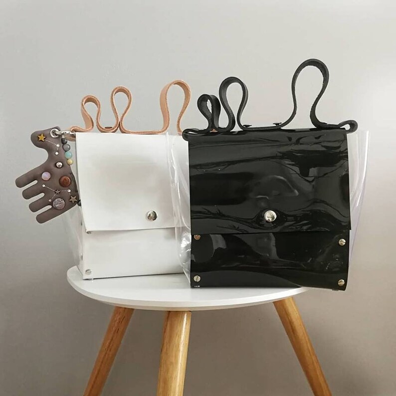 May include: Two clear plastic tote bags with black and white leather accents. The black bag has a black leather flap and the white bag has a white leather flap. Both bags have a leather handle.