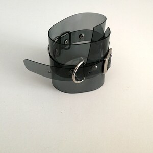 May include: A black plastic choker with a silver buckle and a silver ring. The choker is translucent and has a shiny finish.