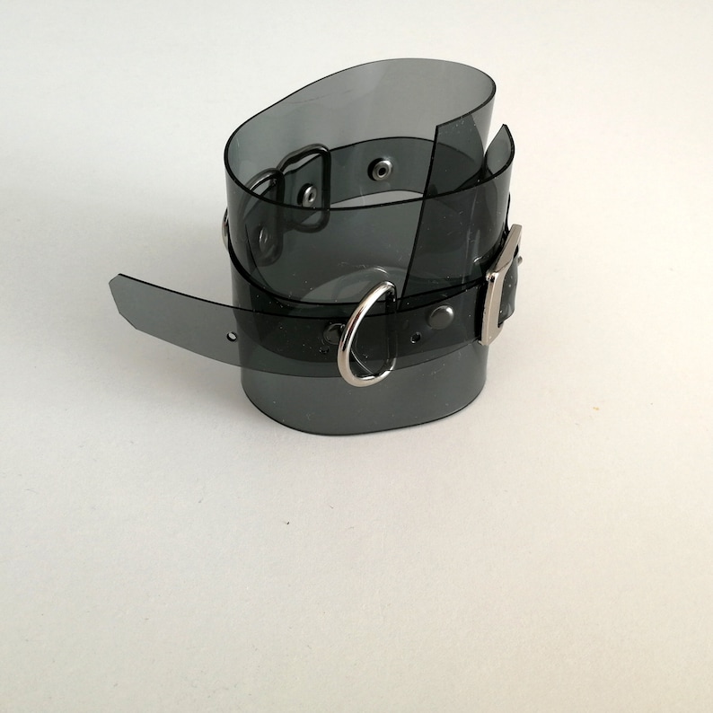 May include: A black plastic choker with a silver buckle and a silver ring. The choker is translucent and has a shiny finish.