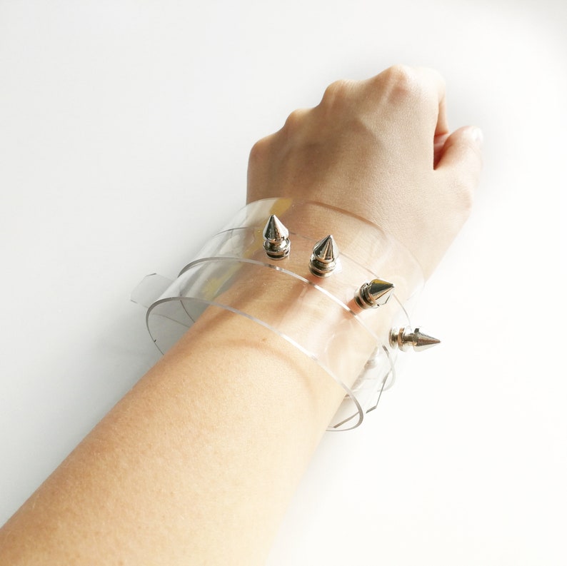 May include: A clear plastic bracelet with silver spikes. The bracelet is adjustable and can be worn on any wrist.