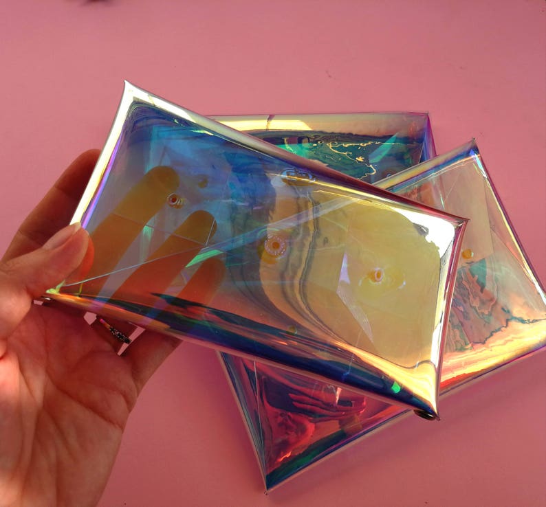 May include: Three iridescent clear plastic pouches stacked on top of each other. The pouches are made of a holographic material that reflects light in a rainbow of colors.