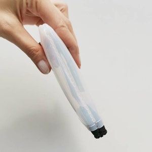 Puede incluir: Un limpiador de brochas de maquillaje de silicona blanco transl&uacute;cido con cerdas negras. El limpiador est&aacute; doblado por la mitad y se sostiene en una mano.