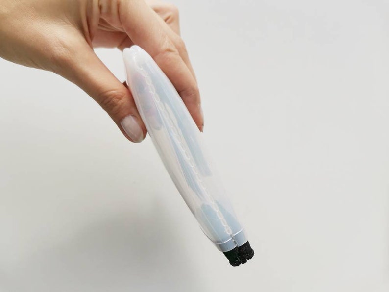 Puede incluir: Un limpiador de brochas de maquillaje de silicona blanco transl&uacute;cido con cerdas negras. El limpiador est&aacute; doblado por la mitad y se sostiene en una mano.