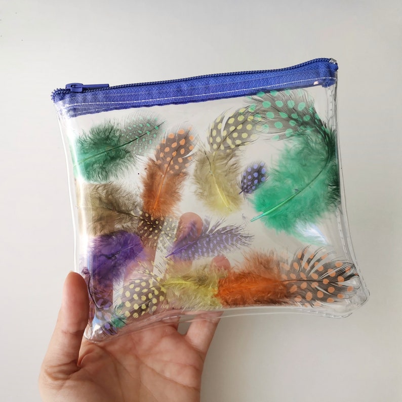 Puede incluir: Bolsa de pl&aacute;stico transparente con cremallera azul y plumas de colores con lunares en el interior.