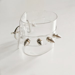 May include: A clear plastic choker with silver spikes. The choker has a clasp closure.