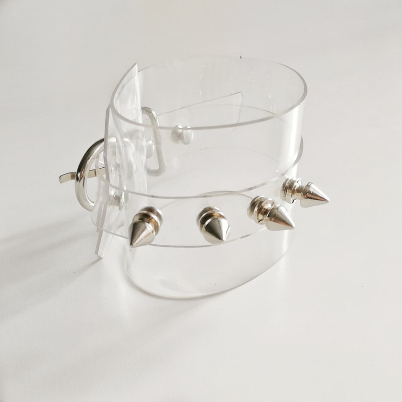 May include: A clear plastic choker with silver spikes. The choker has a clasp closure.