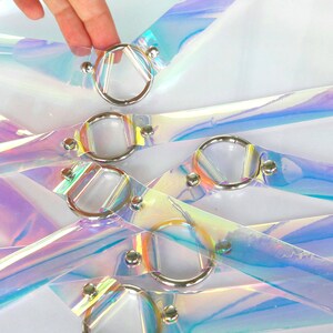 May include: Multiple iridescent clear plastic straps with silver metal rings. The straps are layered and crisscrossed, creating a decorative pattern.