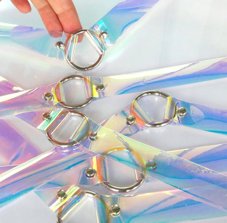 May include: Multiple iridescent clear plastic straps with silver metal rings. The straps are layered and crisscrossed, creating a decorative pattern.